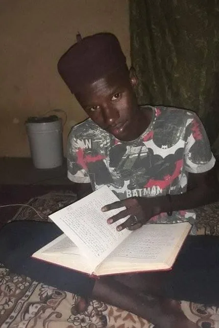 Mouhamed Nour All-Haqq adolescent, étudiant un livre le soir, assis sur un tapis